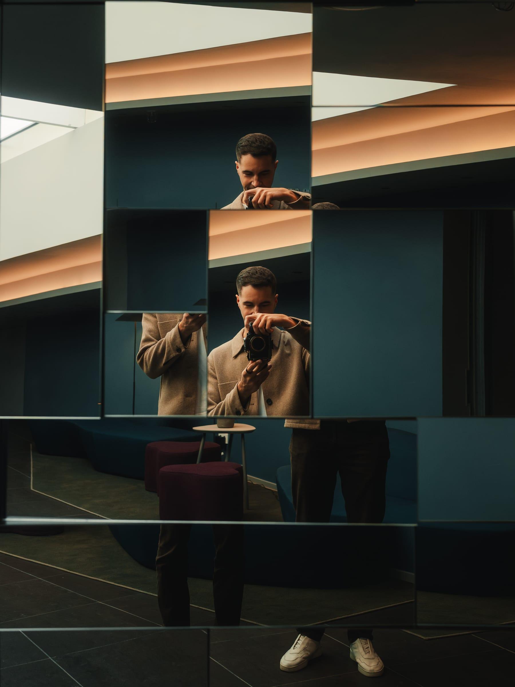 A photographer multiplied across a mirrored wall, camera to his eye