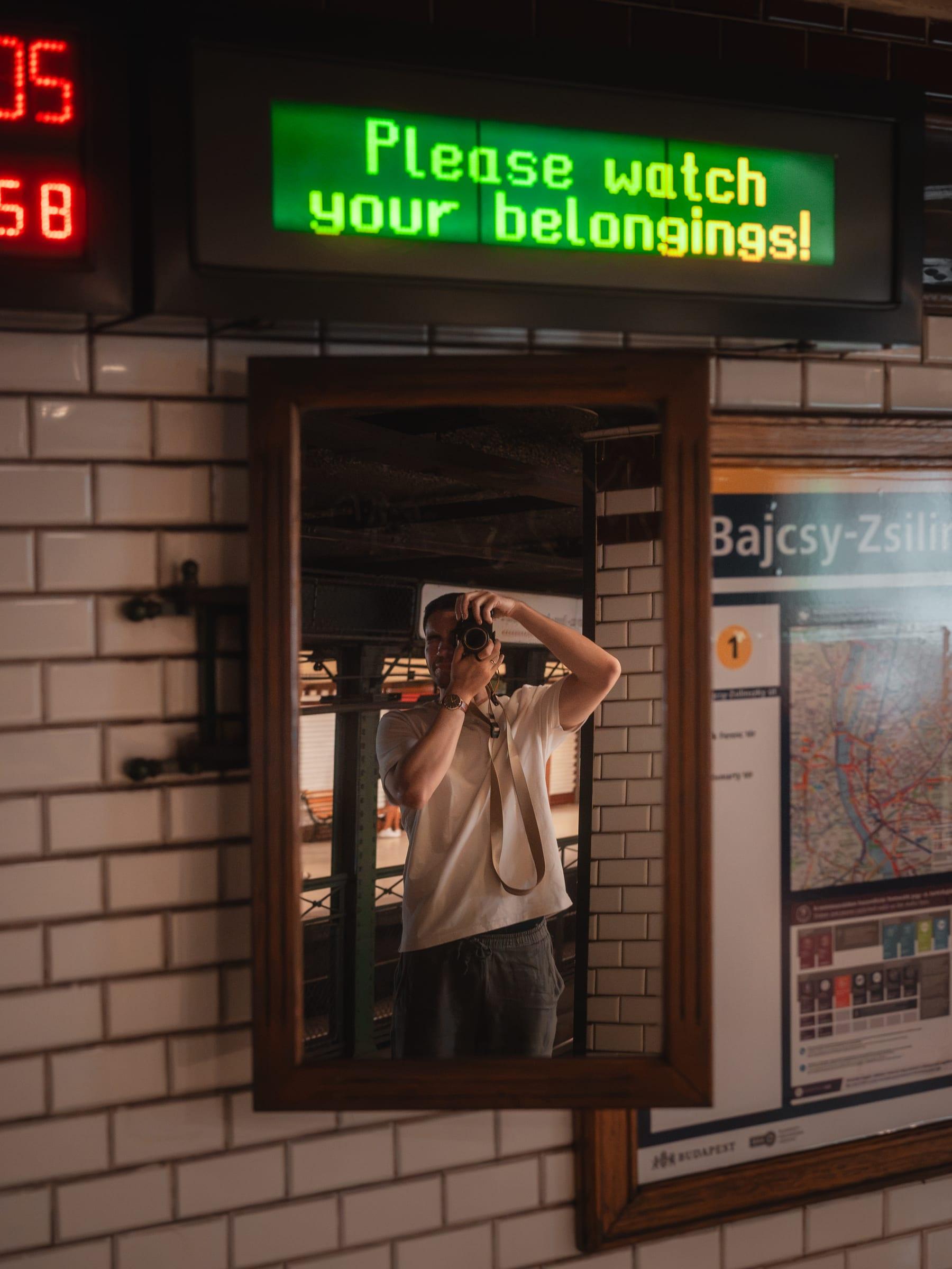 A photographer reflected in a mirror on a tiled metro platform
