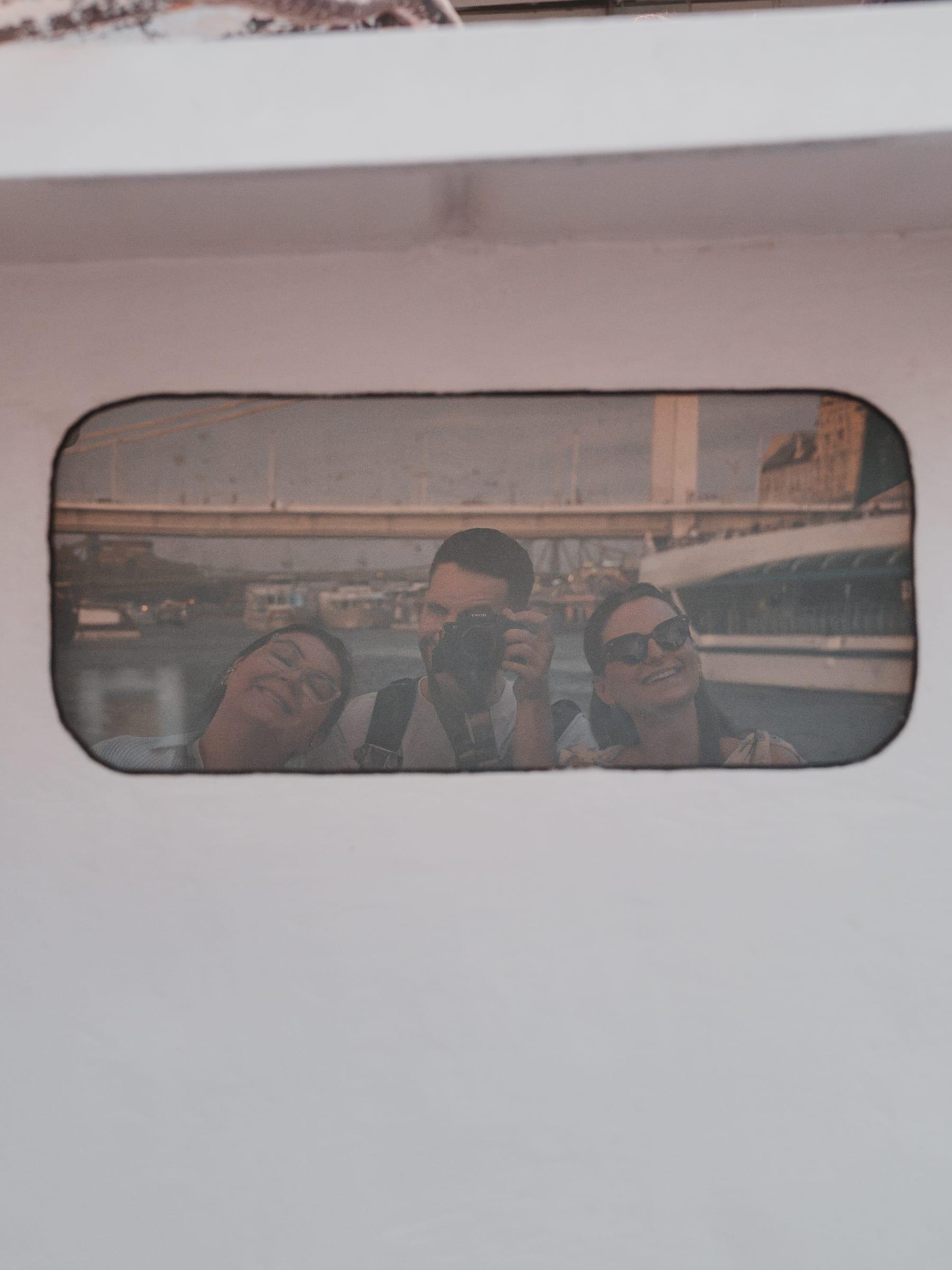 Three of the crew reflected in a boat window, a bridge passing behind