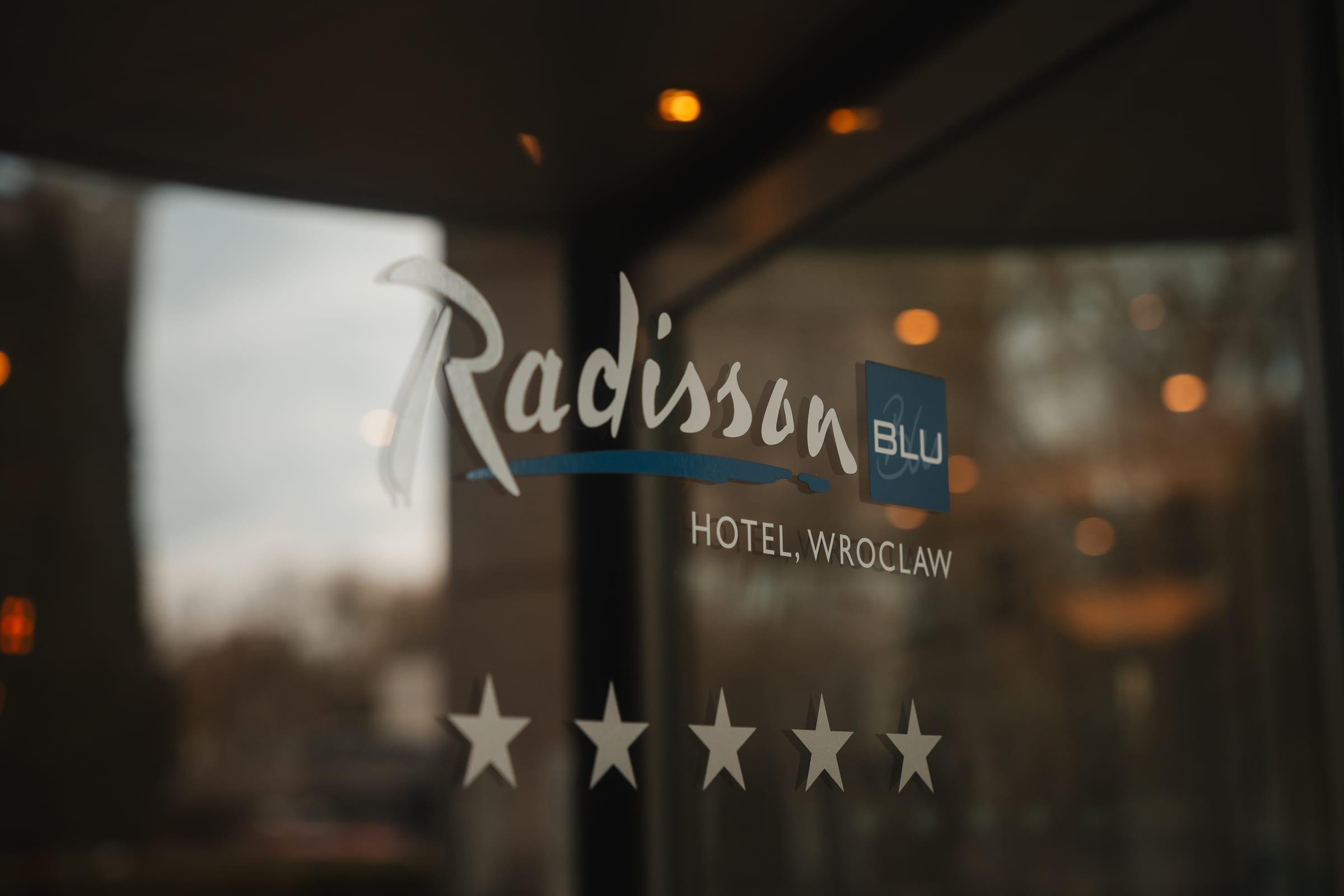 The hotel mark etched into the entrance glass, the street behind it out of focus