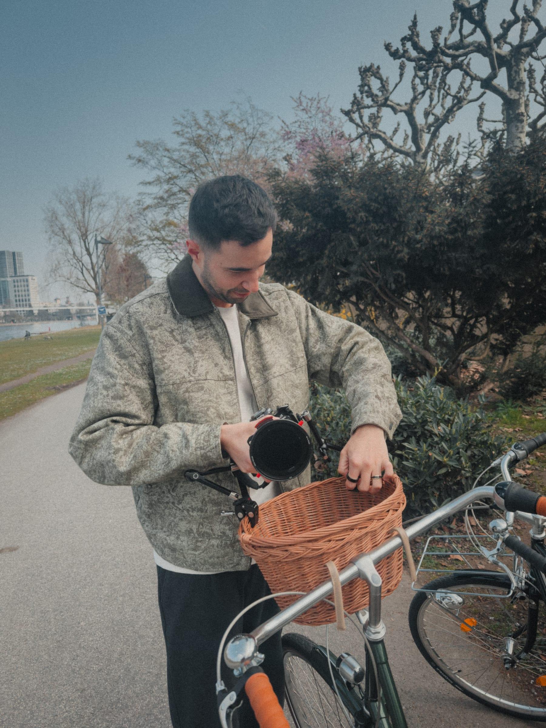 Lowering a camera into the wicker basket of the bicycle on the river path