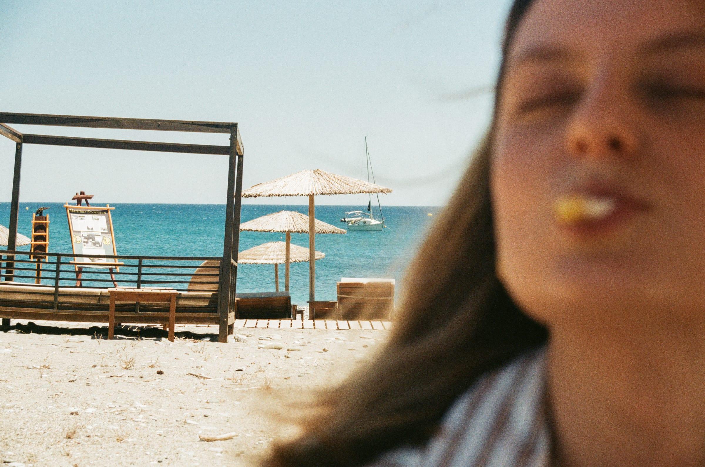 Close in on the beach, mid-mouthful, the umbrellas and a sail out behind