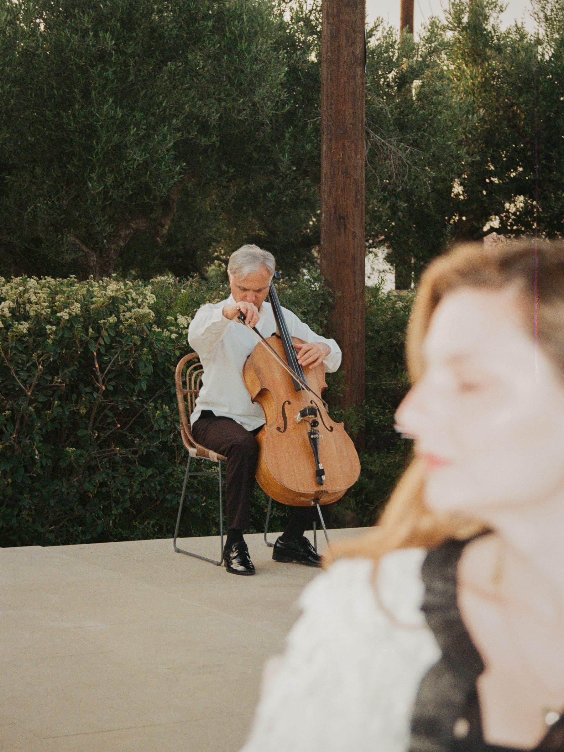 The cellist working through a piece under the trees while we watch from closer in