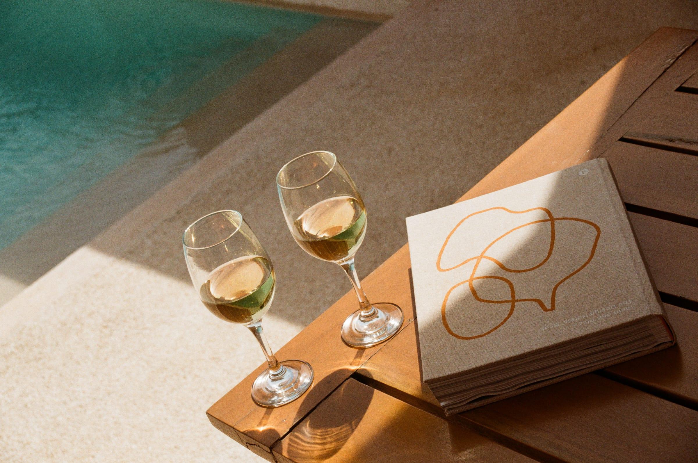 Two glasses of white and a folder set down on the warm stone at the pool edge
